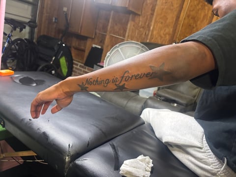Person displaying arm tattoo reading Nothing is Forever in a garage setting