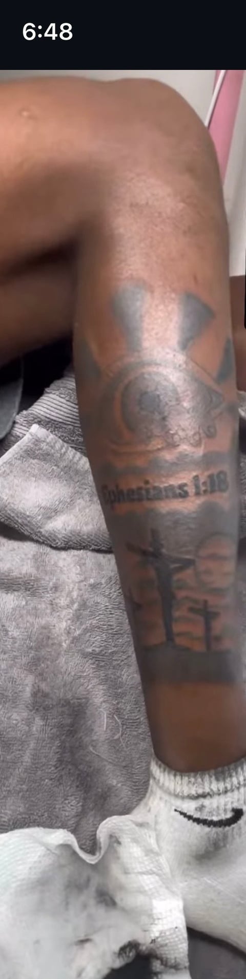 Close-up of a persons arm displaying multiple tattoos including a portrait and text, wearing white socks