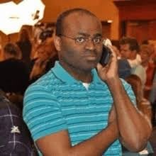 Man wearing turquoise striped shirt talking on phone at indoor event with people in background