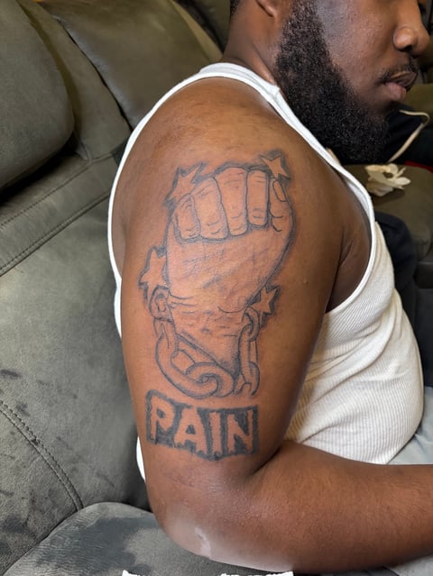 Man displaying arm tattoo of a clenched fist with decorative bands and the word PAIN written below