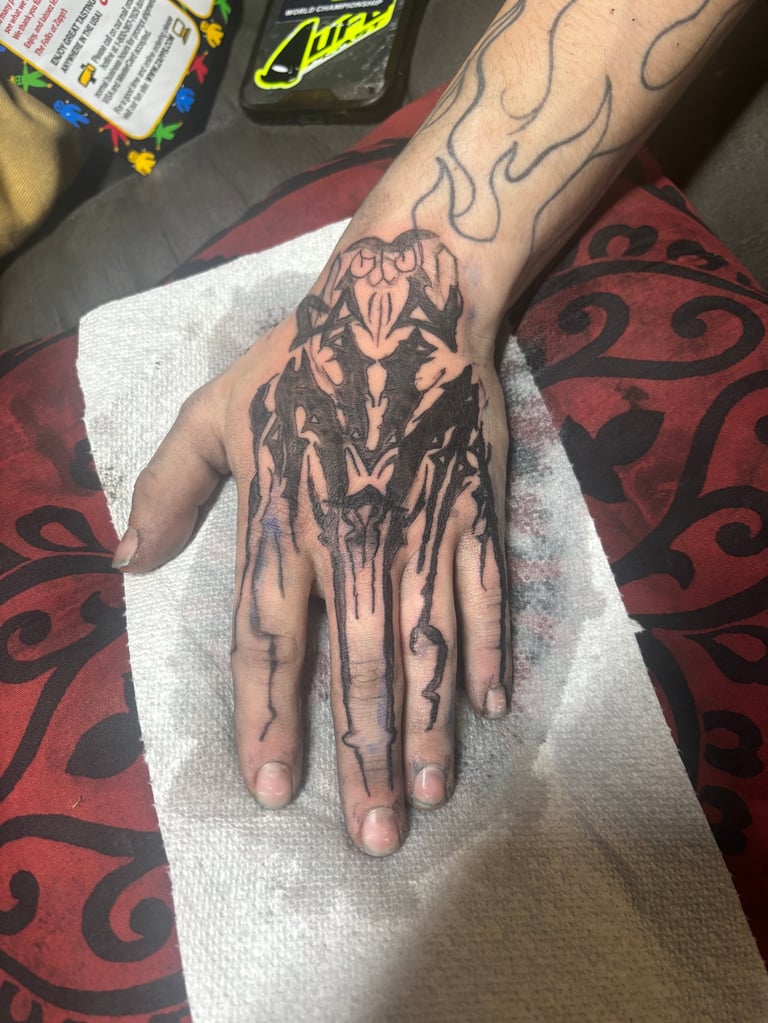 Hand tattoo of a demon or monster face with dripping ink effect on fingers