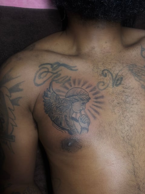 Close-up of male chest showing multiple black tattoos including a winged figure with radiating lines in the center