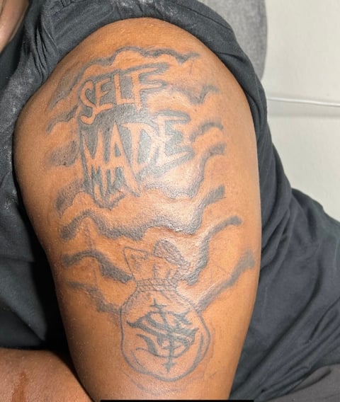 Arm tattoo displaying self-made design with text and decorative symbols on brown skin