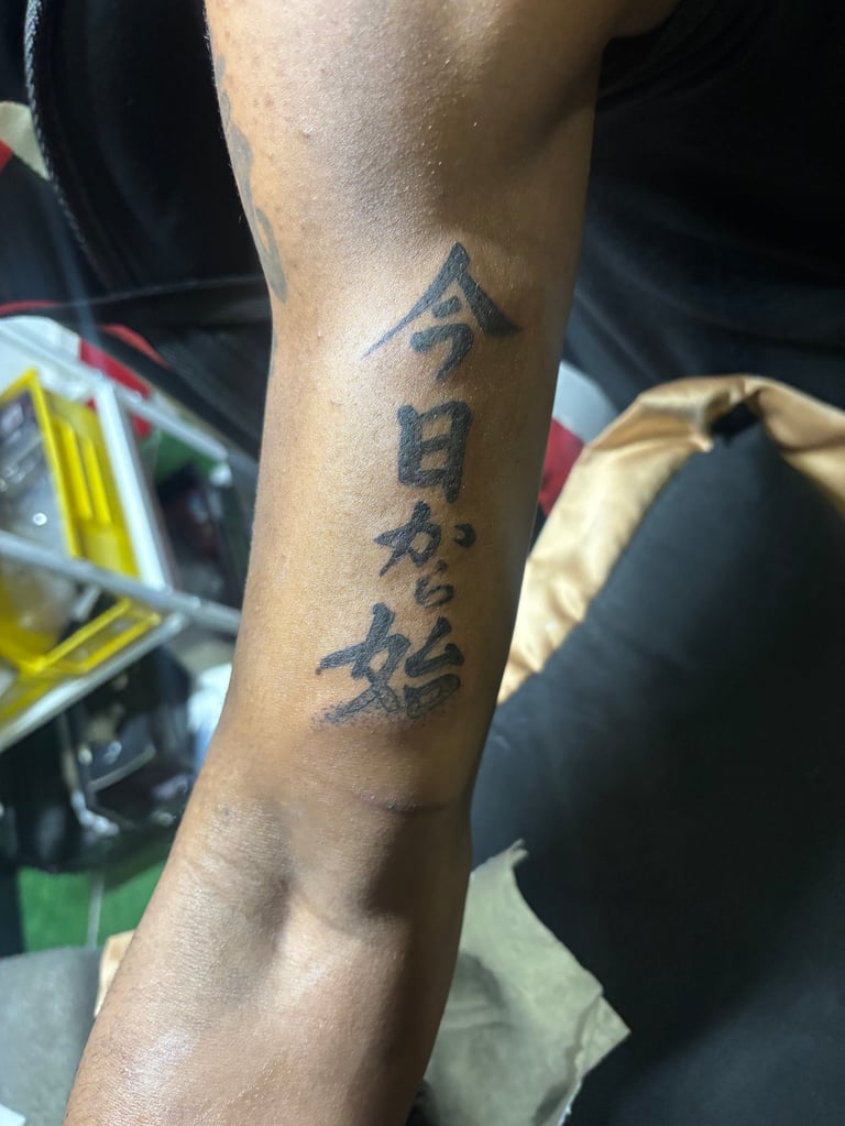 Person showing forearm tattoo with Japanese or Chinese characters in black ink on tanned skin